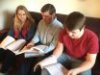 Three people sitting on couch holding open books